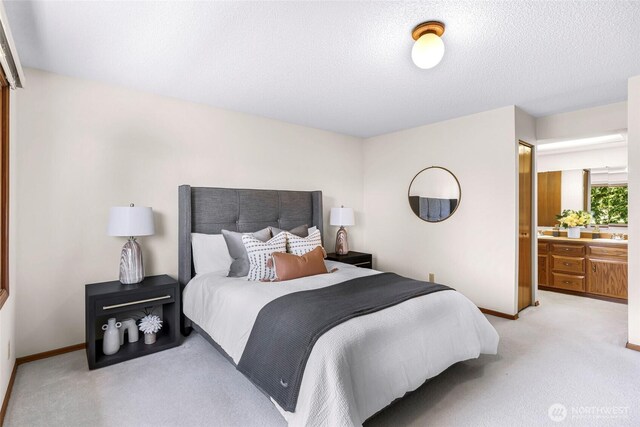 bedroom featuring a textured ceiling, baseboards, light colored carpet, and ensuite bathroom