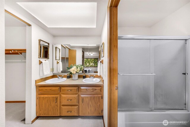 full bathroom with double vanity, a sink, and bath / shower combo with glass door