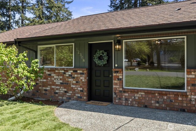view of exterior entry featuring brick siding, a shingled roof, and board and batten siding