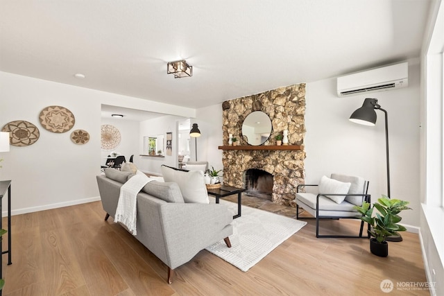 living area with baseboards, a wall unit AC, light wood-type flooring, and a stone fireplace