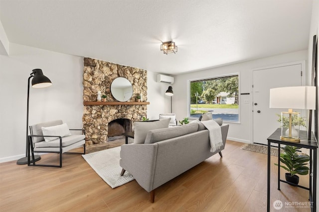 living room featuring baseboards, a stone fireplace, light wood-type flooring, and a wall mounted air conditioner