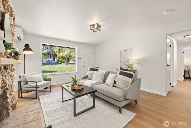 living area featuring a textured ceiling, baseboards, a wall unit AC, and light wood-style flooring