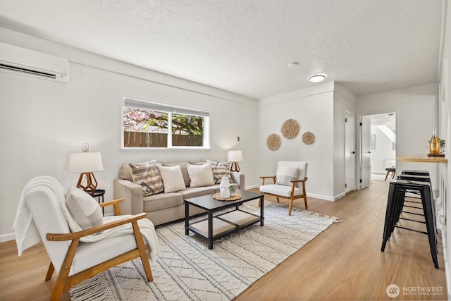 living area featuring baseboards, a wall mounted AC, light wood-type flooring, and a textured ceiling