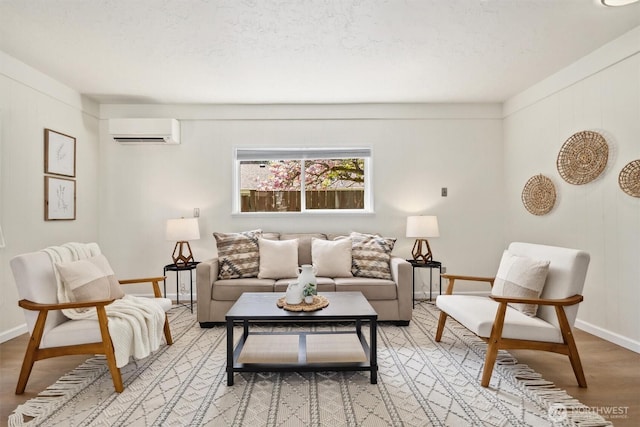 living area featuring baseboards, an AC wall unit, light wood finished floors, and a textured ceiling
