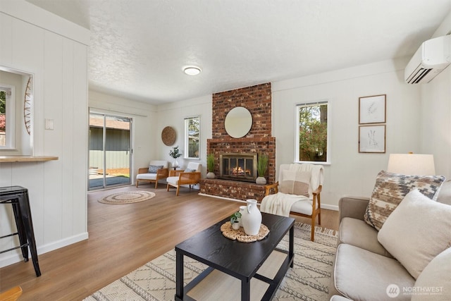 living area with wood finished floors, baseboards, a brick fireplace, and a wall unit AC