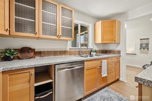 kitchen with stainless steel dishwasher, light brown cabinets, light wood-type flooring, light countertops, and a sink
