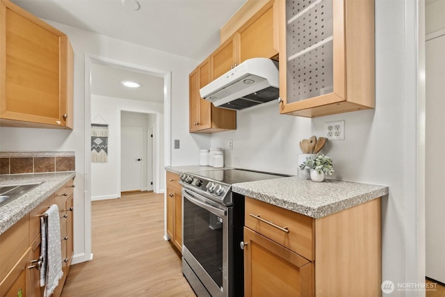 kitchen featuring electric range, light countertops, light wood-style flooring, under cabinet range hood, and glass insert cabinets