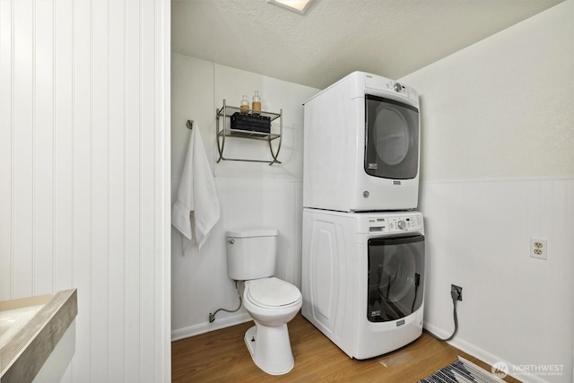 bathroom featuring wood finished floors, stacked washer / drying machine, and toilet