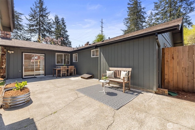 back of property with fence, outdoor dining space, a shingled roof, a chimney, and a patio