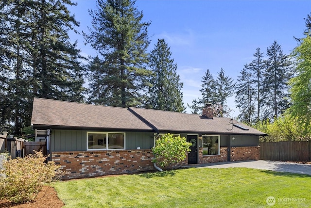 view of front facade with a chimney, brick siding, fence, a front lawn, and a shingled roof
