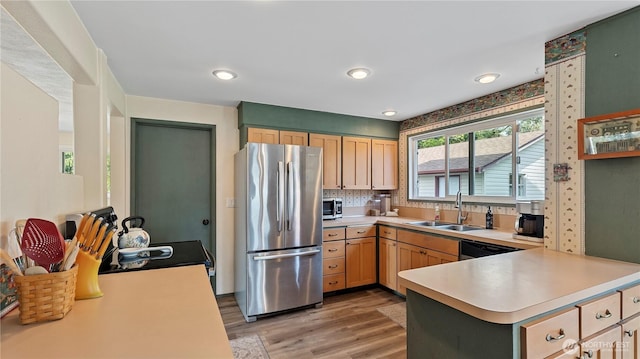 kitchen featuring stainless steel appliances, light countertops, light wood finished floors, a sink, and a peninsula