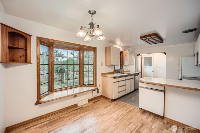 kitchen featuring a sink, light wood-style floors, light countertops, freestanding refrigerator, and baseboards