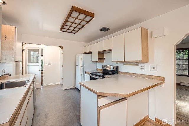 kitchen with electric range, a sink, baseboards, freestanding refrigerator, and a peninsula