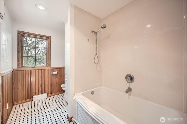 full bathroom with wooden walls, a wainscoted wall, shower / bathtub combination, and toilet