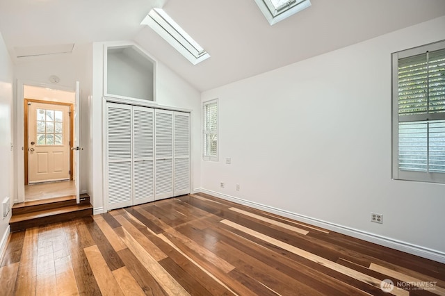 unfurnished bedroom with a closet, baseboards, lofted ceiling with skylight, and hardwood / wood-style floors