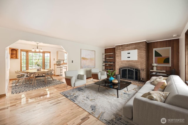 living area with arched walkways, a fireplace, light wood-type flooring, baseboards, and a chandelier