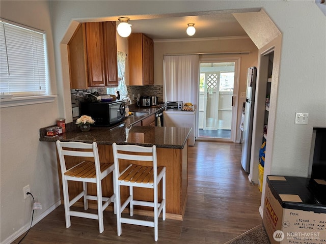 kitchen with a sink, black microwave, dark countertops, dark wood-style flooring, and brown cabinetry