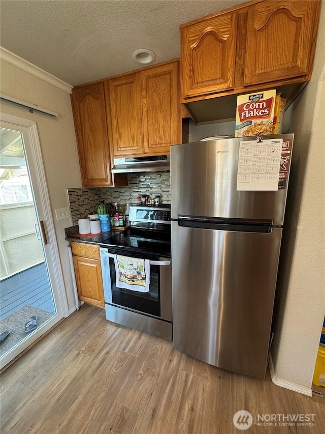 kitchen featuring stainless steel appliances, light wood-style floors, under cabinet range hood, backsplash, and ornamental molding