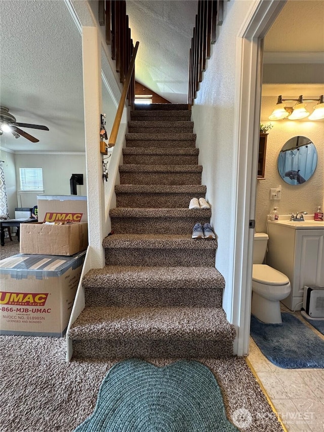 stairs with ceiling fan, a textured ceiling, and crown molding
