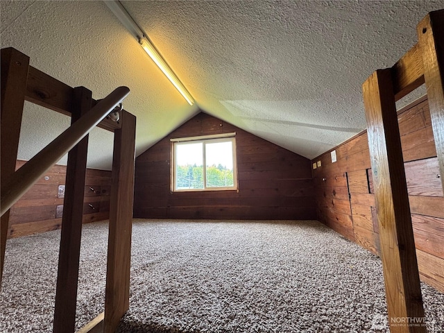 bonus room with wood walls, a textured ceiling, carpet, and vaulted ceiling