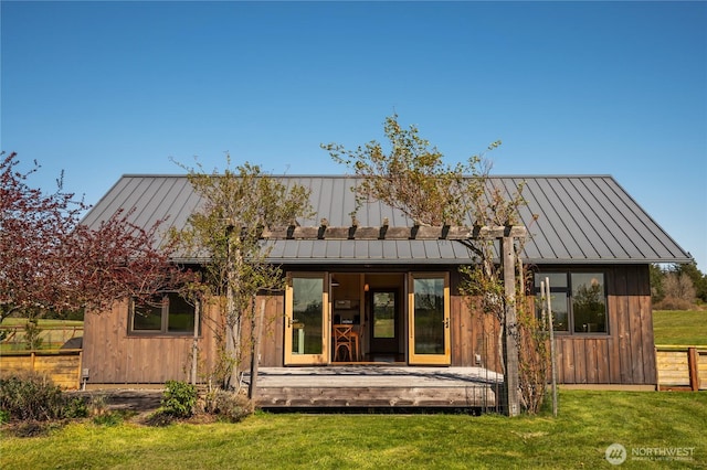 back of house featuring a deck, a standing seam roof, metal roof, and a lawn