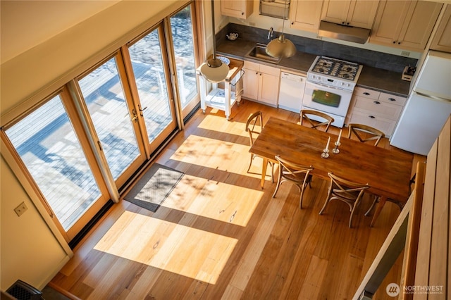 kitchen with light wood-type flooring, dark countertops, white appliances, and a sink