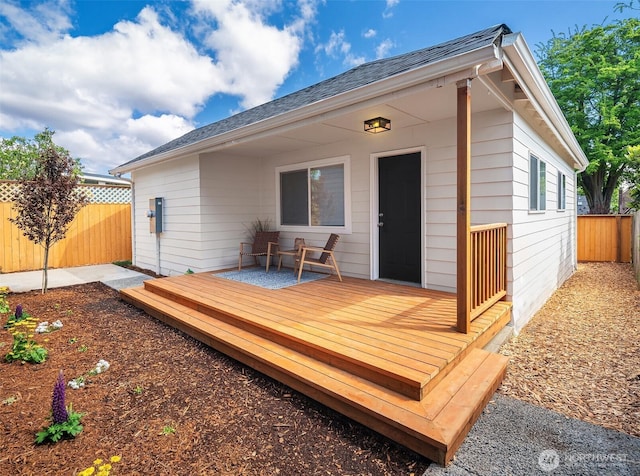 rear view of house with fence, a wooden deck, and roof with shingles