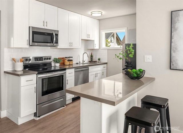 kitchen with decorative backsplash, light wood-style flooring, a sink, stainless steel appliances, and a kitchen bar