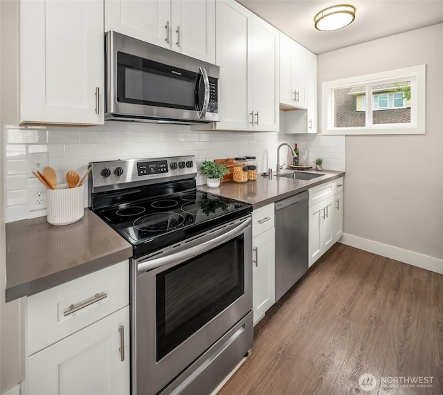 kitchen with stainless steel appliances, a sink, dark countertops, white cabinetry, and dark wood-type flooring