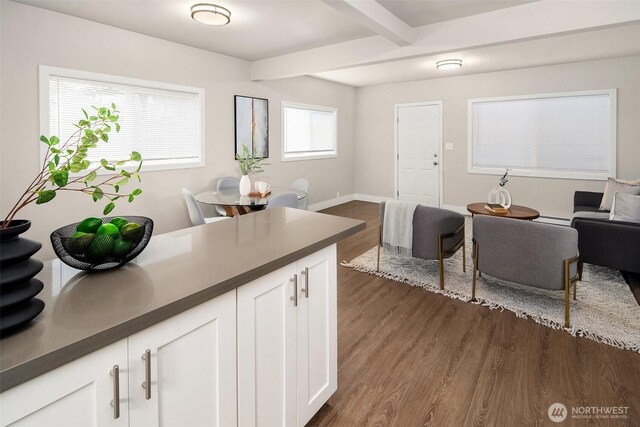 kitchen with dark wood finished floors, beamed ceiling, dark countertops, white cabinetry, and open floor plan