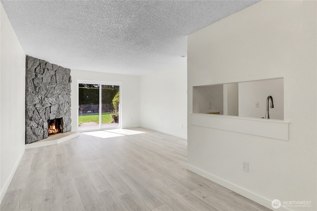 21615 80th Ave W Unit 101, Edmonds, WA 98026 - unfurnished living room featuring baseboards, a textured ceiling, wood finished floors, and a stone fireplace