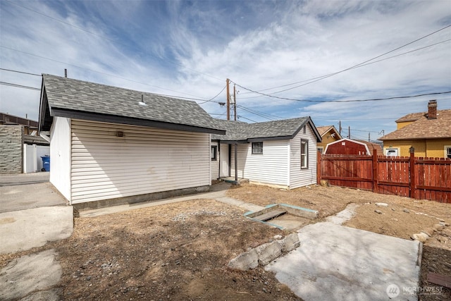 rear view of property featuring fence and roof with shingles