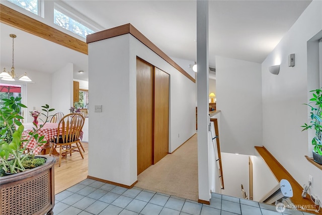 hall with an upstairs landing, light tile patterned floors, healthy amount of natural light, and light colored carpet