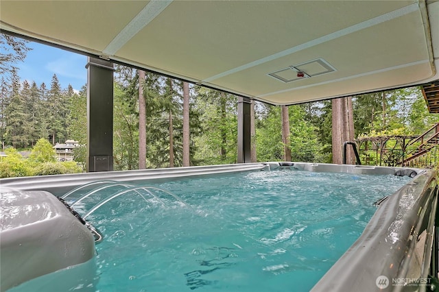 view of swimming pool featuring a hot tub and view of wooded area