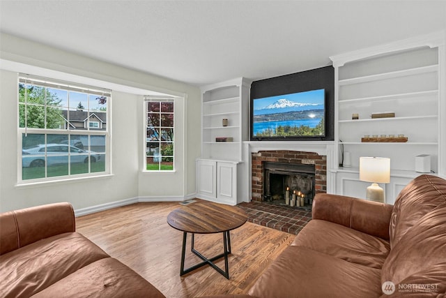 living area featuring visible vents, built in features, wood finished floors, a fireplace, and baseboards