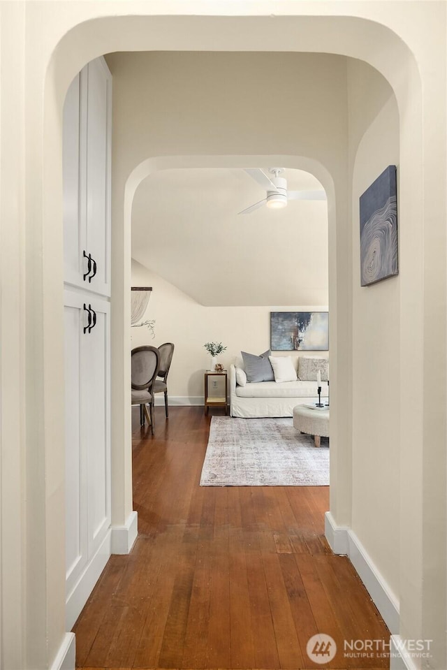 hallway with dark wood-type flooring, arched walkways, and baseboards