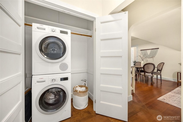 clothes washing area featuring stacked washer and dryer, laundry area, baseboards, and dark wood-type flooring
