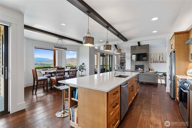 kitchen featuring dark wood finished floors, a large fireplace, appliances with stainless steel finishes, beam ceiling, and open floor plan