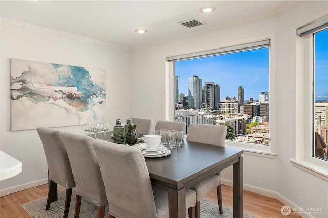 dining room with plenty of natural light, visible vents, crown molding, wood finished floors, and baseboards