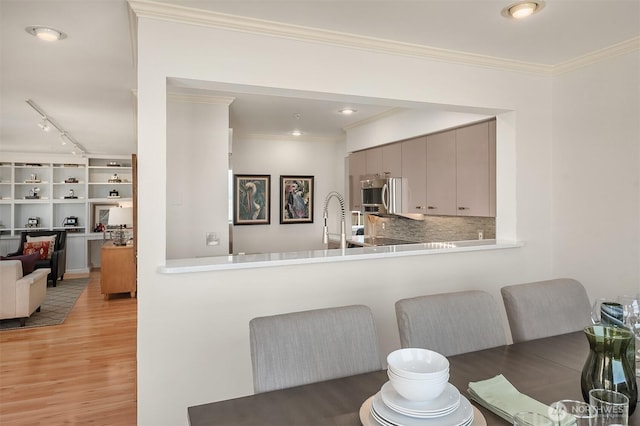 kitchen featuring track lighting, ornamental molding, a peninsula, tasteful backsplash, and light wood finished floors