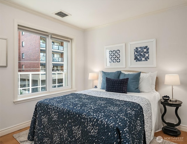bedroom featuring visible vents, baseboards, crown molding, and wood finished floors