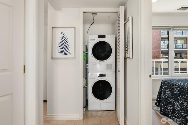 laundry area with laundry area, visible vents, baseboards, tile patterned floors, and stacked washer / drying machine