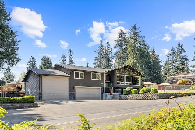 view of front of home featuring fence, driveway, stone siding, and a garage