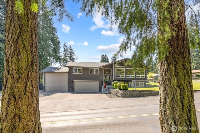 bi-level home featuring an attached garage, concrete driveway, and stone siding