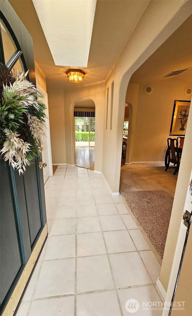 hallway with baseboards, arched walkways, and light tile patterned floors