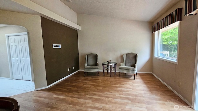 living area with arched walkways, wood finished floors, and vaulted ceiling