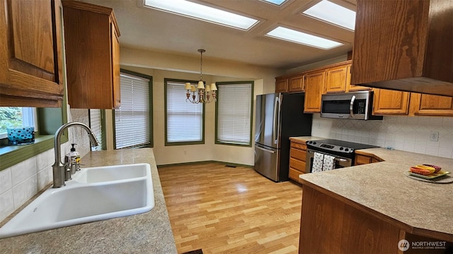 kitchen with decorative backsplash, light wood-style floors, a chandelier, a sink, and stainless steel appliances