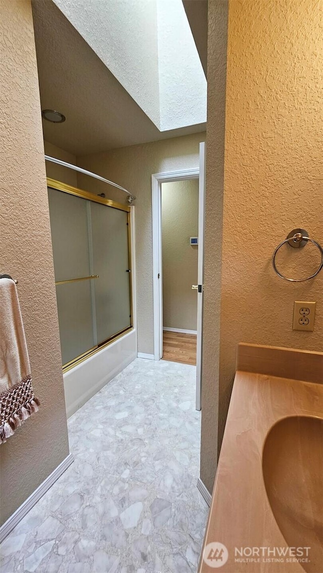 full bath with tile patterned floors, a textured wall, baseboards, and shower / bath combination with glass door