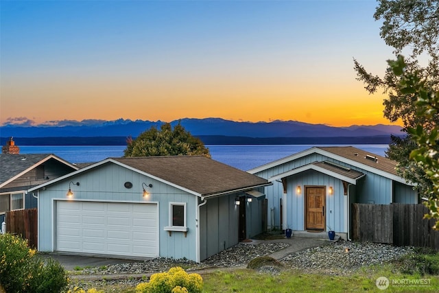 view of front facade with a garage, a mountain view, fence, and a shingled roof