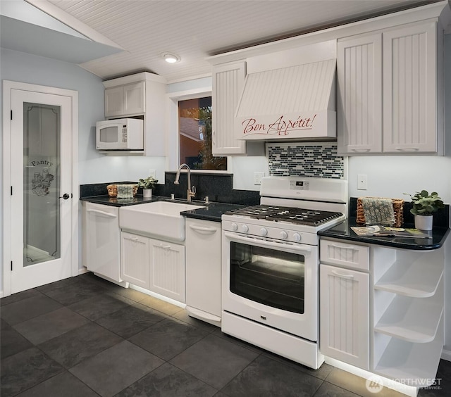 kitchen with a sink, dark countertops, premium range hood, dark tile patterned flooring, and white appliances
